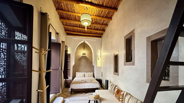 A narrow hallway leading to a bedroom with a bed, a bench, and a small table. - Riad Sakura Marrakech  (Marrakech)