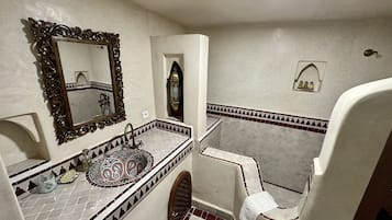 A bathroom with a large ornate mirror, a sink with a patterned tile backsplash, and a towel rack.