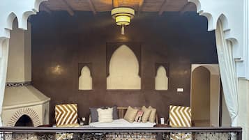 A room with a bed, decorative pillows, a chandelier, and a balcony with wrought iron railings.
