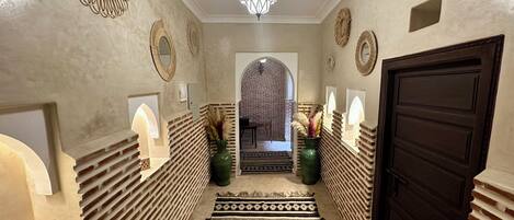 A hallway with patterned rugs, decorative mirrors, and a geometric light fixture.