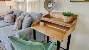 Ein gemütliches Wohnzimmer mit grauem Sofa, gestreiften Kissen, einem Holznachttisch mit Spiegel, einer kleinen Pflanze und einem grünen Sessel.