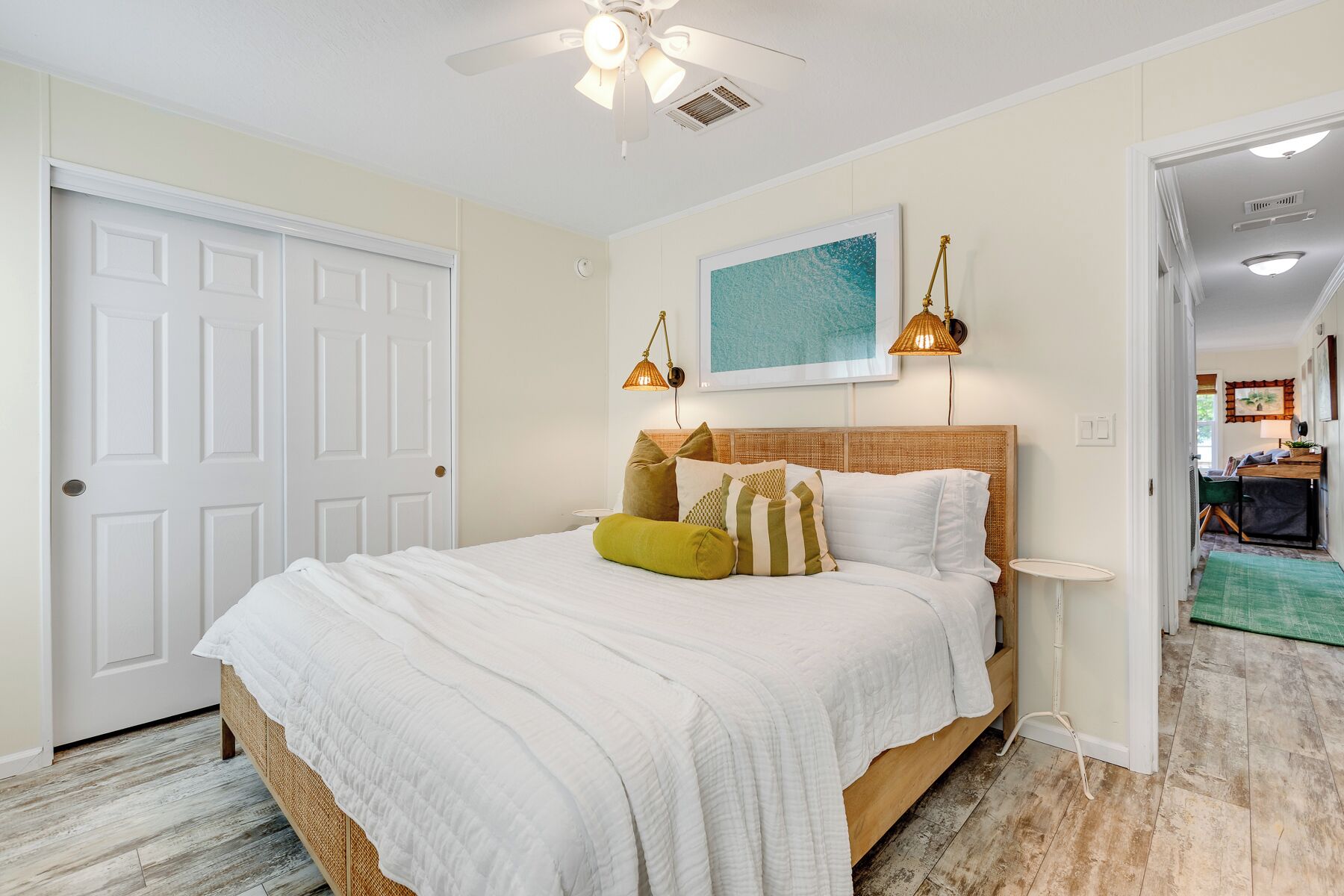 Une chambre à coucher avec un lit, un ventilateur de plafond, un tableau et une porte.