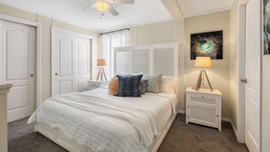 Une chambre à coucher comprenant un lit, des tables de chevet, un ventilateur de plafond et une lampe fixée au mur.