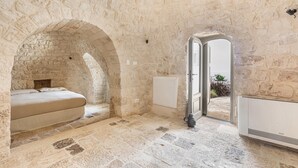 A stone-walled room with a bed, a radiator, and an open doorway leading outside. - 3643 Masseria Stella del Monte by Perle di Puglia (Cisternino)