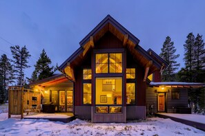 A modern log cabin with large windows, a covered porch, and a snow-covered ground.
