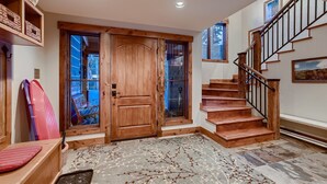 Una escalera de madera con barandilla de metal, una puerta de madera y vistas al exterior a través de un ventanal.