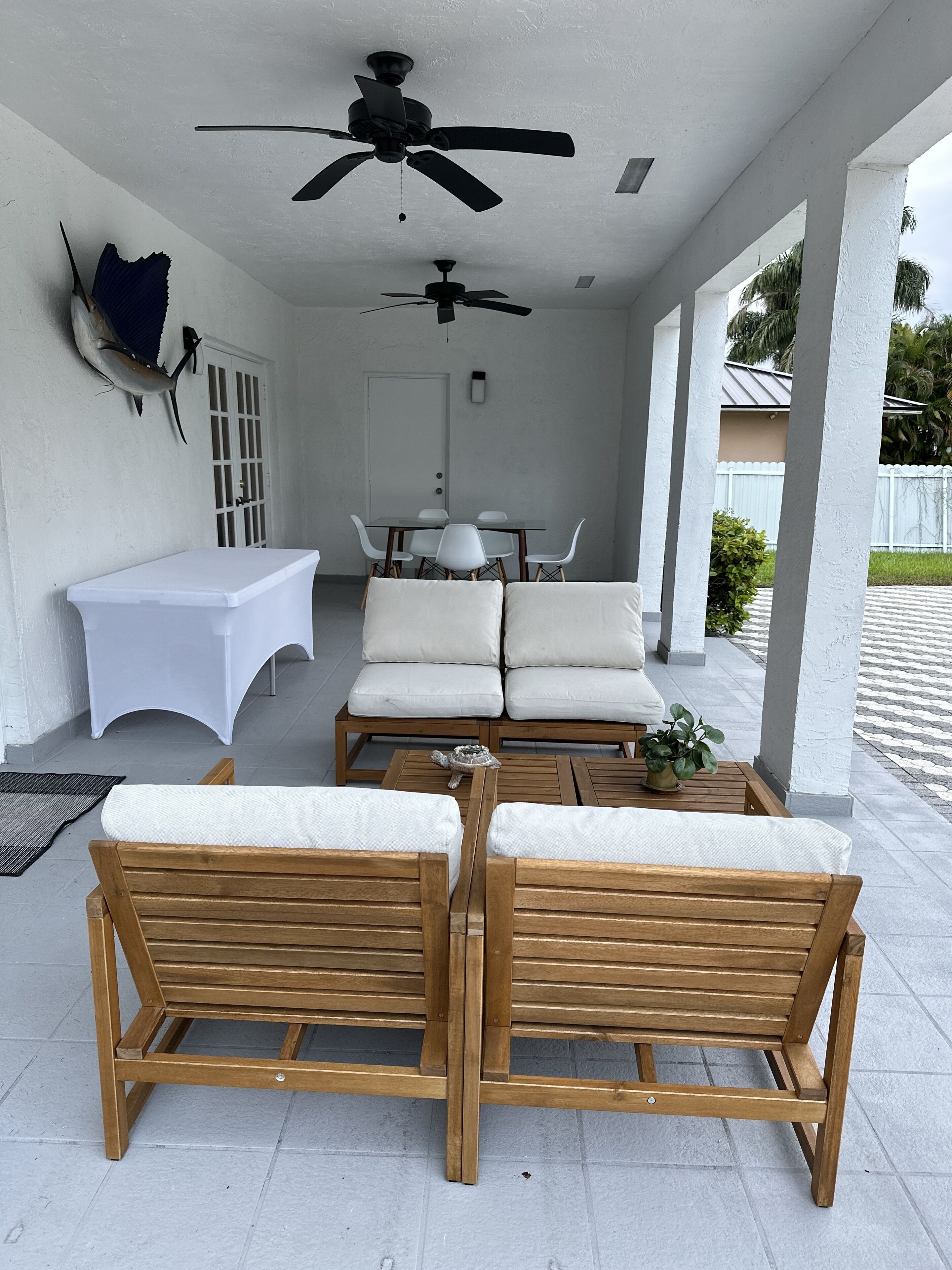 A covered patio area with two wooden lounge chairs, a small table, and a ceiling fan.