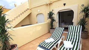 A rooftop terrace with two lounge chairs, a staircase, and potted plants.
