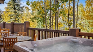 Un jacuzzi en una terraza de madera con sillas, rodeado de árboles con hojas amarillas.