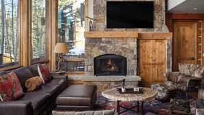 Una sala de estar acogedora con chimenea de piedra, mobiliario de cuero y grandes ventanales con vistas a un bosque.