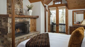 Un dormitorio con chimenea de piedra, techo de madera y una cama grande con una manta marrón.