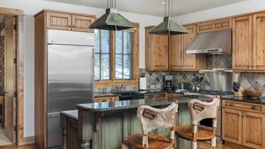 Una cocina con armarios de madera, un refrigerador de acero inoxidable, una isla grande con dos taburetes y una estufa a gas.
