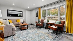 Ein modernes Wohnzimmer mit einer Couch, Sesseln, einem Couchtisch und einem großen Fenster mit Vorhängen.