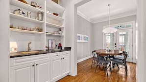 A kitchen with white cabinetry, a wooden countertop, a dining table with chairs, and a pendant light.