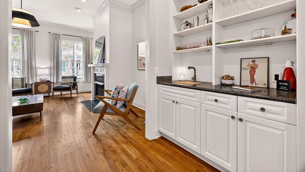A modern kitchen with white cabinets, a black countertop, and a dining area with a wooden table and chairs.