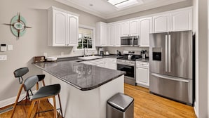A modern kitchen with white cabinetry, a central island, stainless steel appliances, and a clock on the wall.