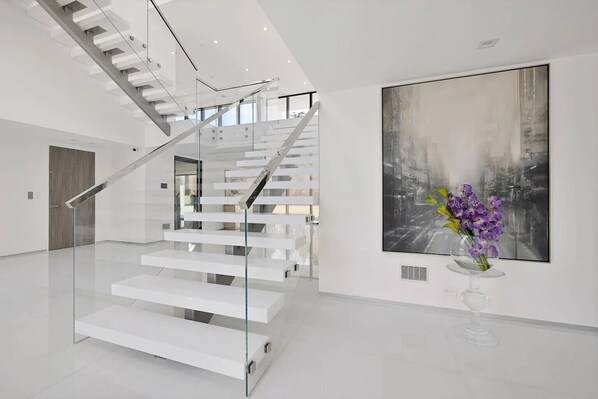 A modern interior with a glass staircase, a large abstract painting, and a vase with flowers. - Newly developed contemporary home situated on 1.5 acres. (Water Mill)
