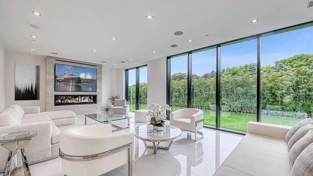 A modern living room with a fireplace, large windows, and a view of a lush garden. - Newly developed contemporary home situated on 1.5 acres. (Water Mill)