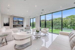 A modern living room with a fireplace, large windows, and a view of a lush garden. - Newly developed contemporary home situated on 1.5 acres. (Water Mill)