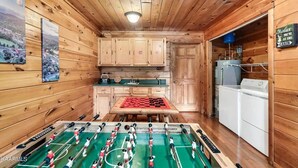 A wooden cabin interior with a foosball table, kitchen cabinets, and a laundry area. - Beautiful & Cozy Amazing Views, Games rm! (Sevierville)