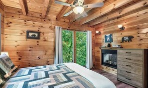 A wooden cabin bedroom with a bed, a fireplace, and a large window with curtains.