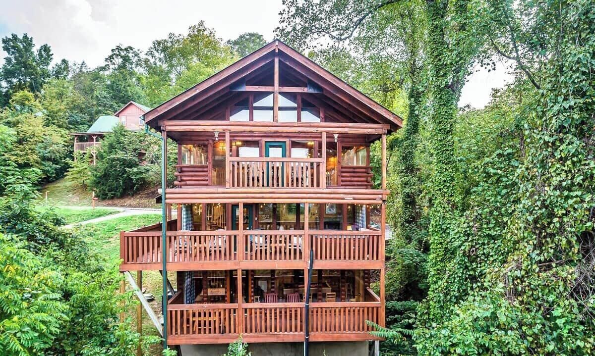 A multi-story wooden cabin with balconies, surrounded by lush greenery.