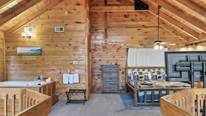 A log cabin interior with a wooden interior, a bed with a headboard, a fireplace, a sink, and a ceiling fan. - Beautiful & Cozy Amazing Views, Games rm! (Sevierville)