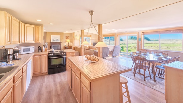 A spacious kitchen with wooden cabinets, a central island, and a dining area with a view of the outdoors. - Hot Tub, Amazing Views, Ocean Front, Pets OK (Serenity) (Ocean Park)