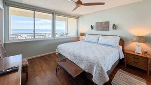 Un dormitorio con cama, escritorio, silla, ventilador de techo, mesita de noche y vistas al océano.
