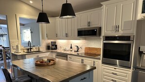 A modern kitchen with white cabinets, a central island, stainless steel appliances, and pendant lighting.