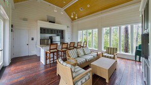 Amplia sala de estar con cocina, ventanas grandes y techo de madera.