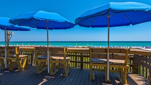 Une terrasse en bois, agrémentée de parasols bleus et de chaises en bois, qui offre une vue sur la plage.
