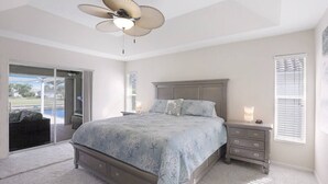 Une chambre à coucher avec un lit, une table de chevet, un ventilateur de plafond et une vue sur l’extérieur.