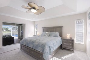 Un dormitorio con cama, mesita de noche, ventilador de techo y vistas al exterior.