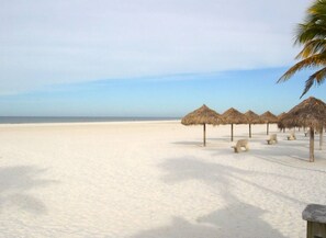 A beach with thatched umbrellas and benches.