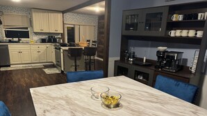 A modern kitchen with white cabinets, a marble countertop, and a coffee station.