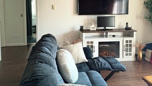A living room with a large sectional sofa, a flat-screen TV mounted on the wall, and a fireplace.