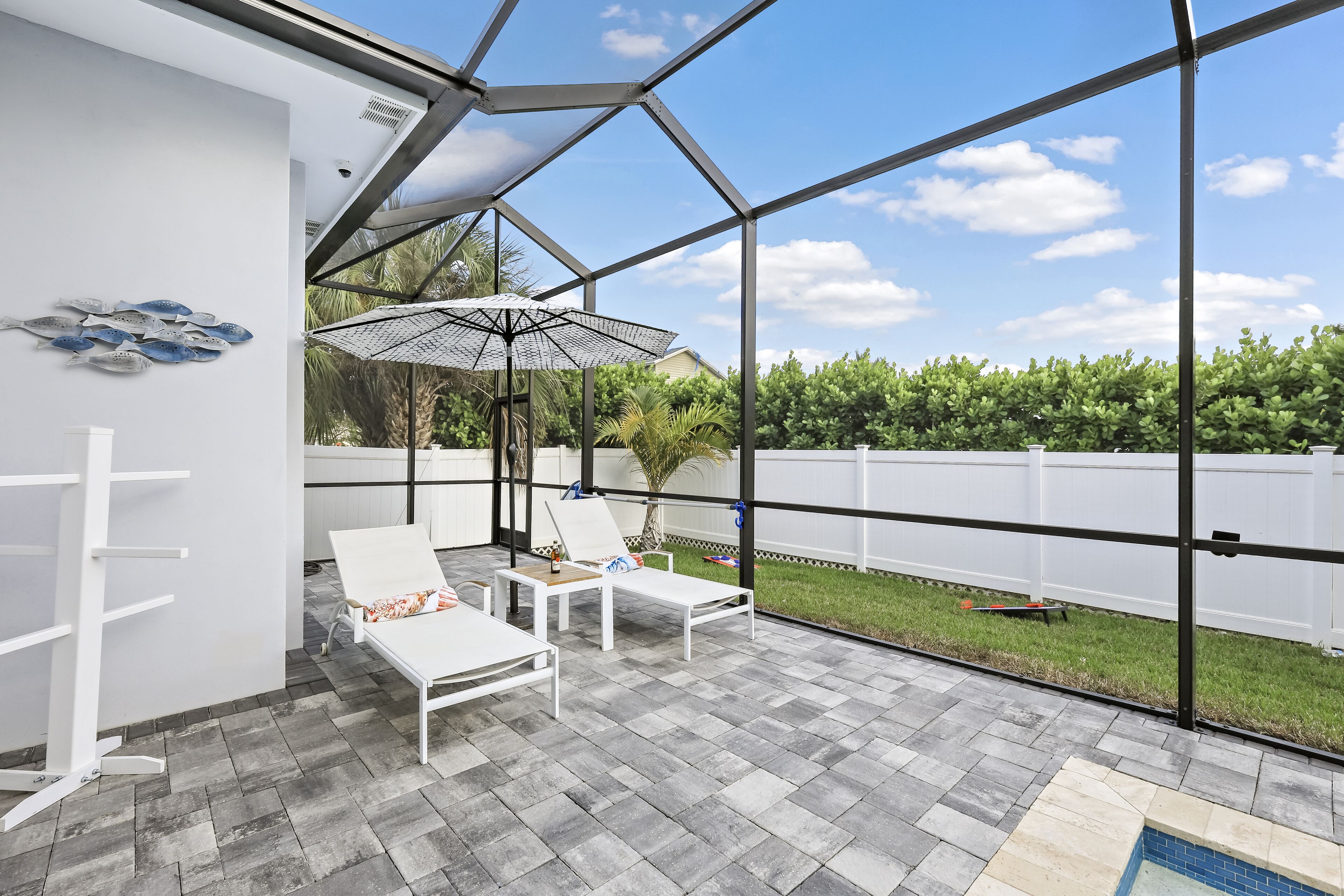 A covered patio with two white lounge chairs, a table, and a large umbrella.