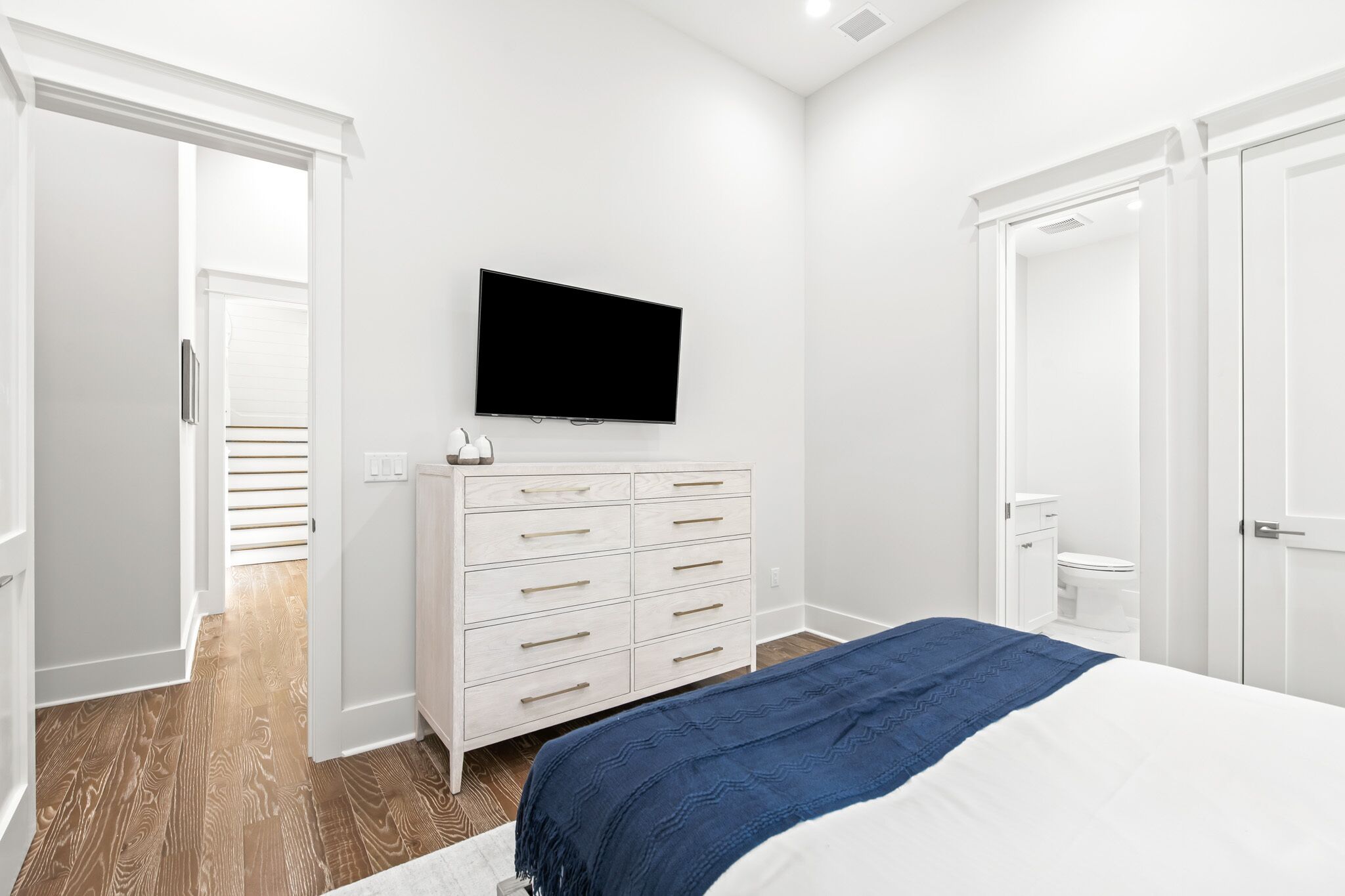 A bedroom with a bed, a dresser, a television, and a bathroom visible through an open door.