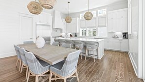 A modern kitchen with white cabinetry, a wooden dining table with wicker chairs, and pendant lights. - Walk to Seaside! Luxury 6BR w/ Private Pool, Golf Cart & Elevator | Sleeps 20 (Santa Rosa Beach)
