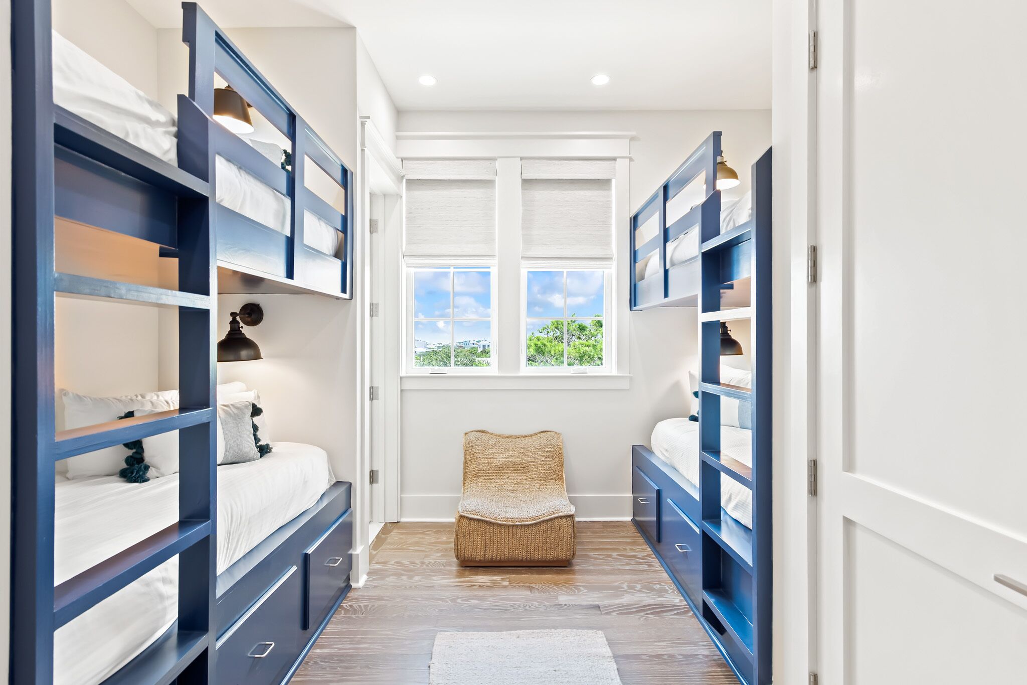 A narrow room with bunk beds, a woven chair, and a window with a view.
