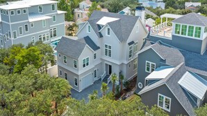 A residential area with multiple houses, including a large two-story house with a covered patio and a swimming pool. - Walk to Seaside! Luxury 6BR w/ Private Pool, Golf Cart & Elevator | Sleeps 20 (Santa Rosa Beach)
