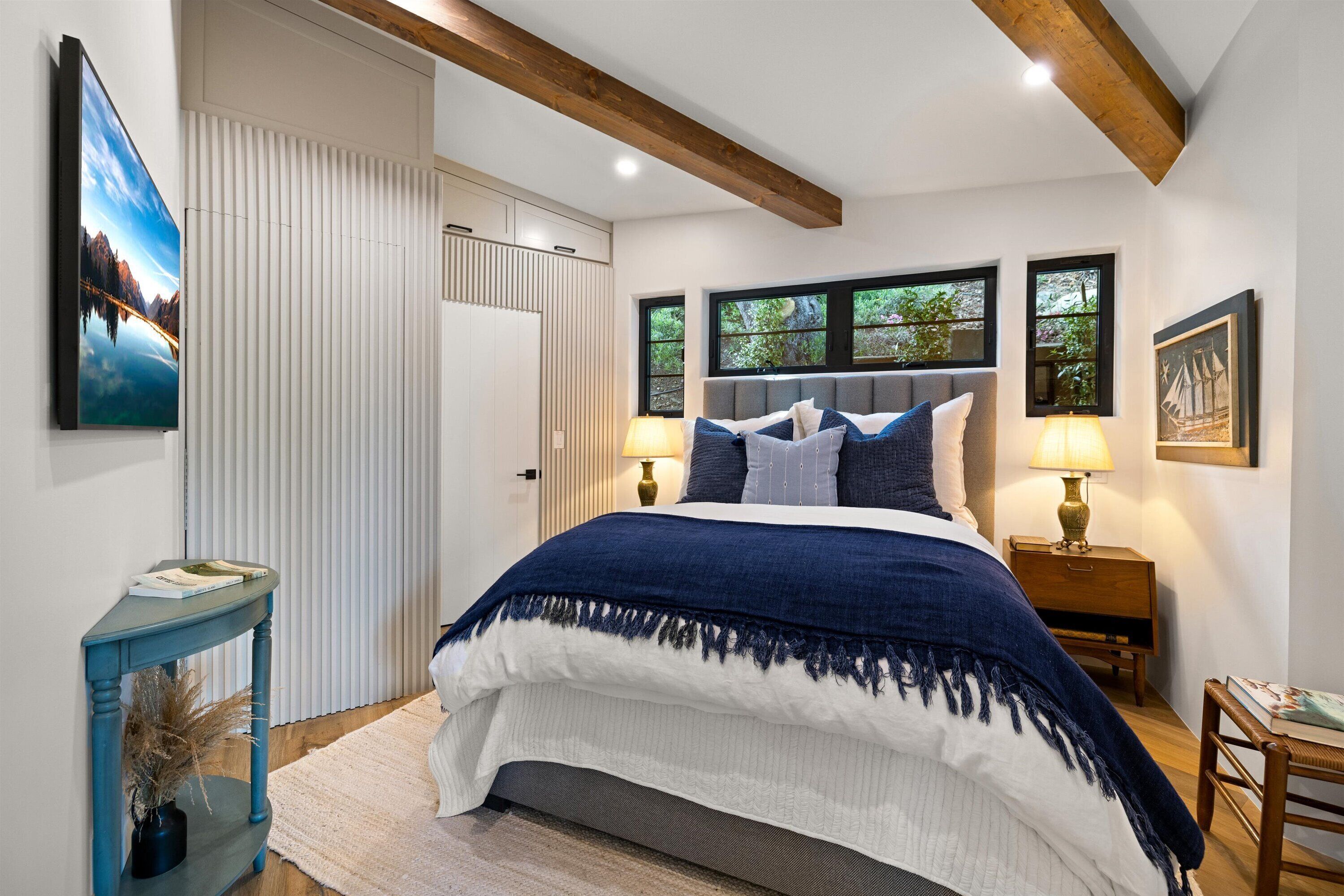A bedroom with a large bed, two bedside lamps, a nightstand, a window with a view, and a door with a white panel.