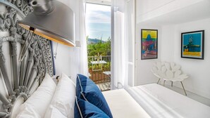 A hotel room with a bed, a white chair, a balcony with a table and chairs, and two framed pictures on the wall. - Iommella Luxury Flat - Adami (Sant'Agnello)