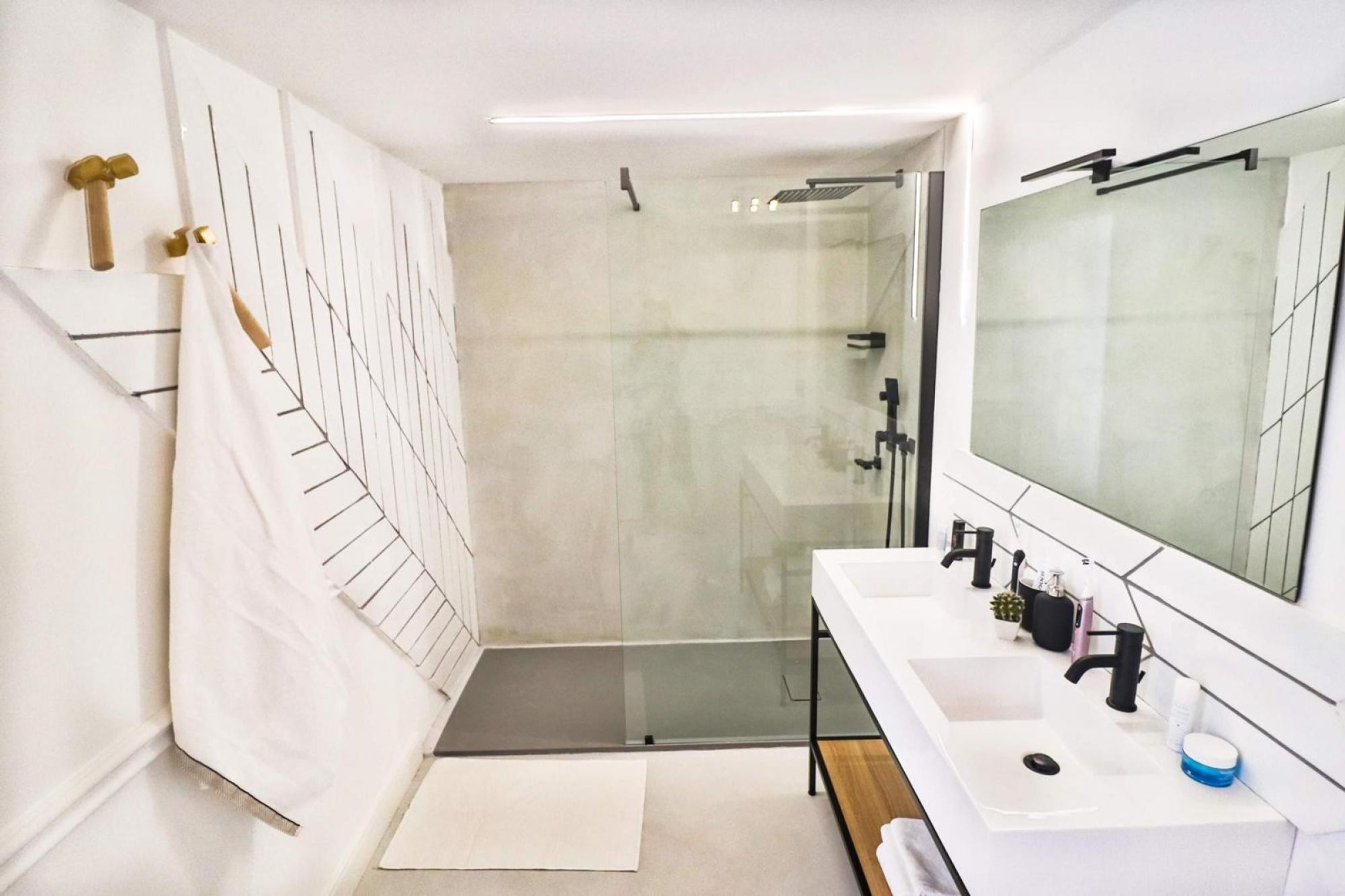Un baño moderno con cabina de ducha de vidrio, un lavabo blanco con un espejo grande y un perchero para toallas.