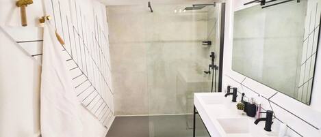 Un baño moderno con cabina de ducha de vidrio, un lavabo blanco con un espejo grande y un perchero para toallas.