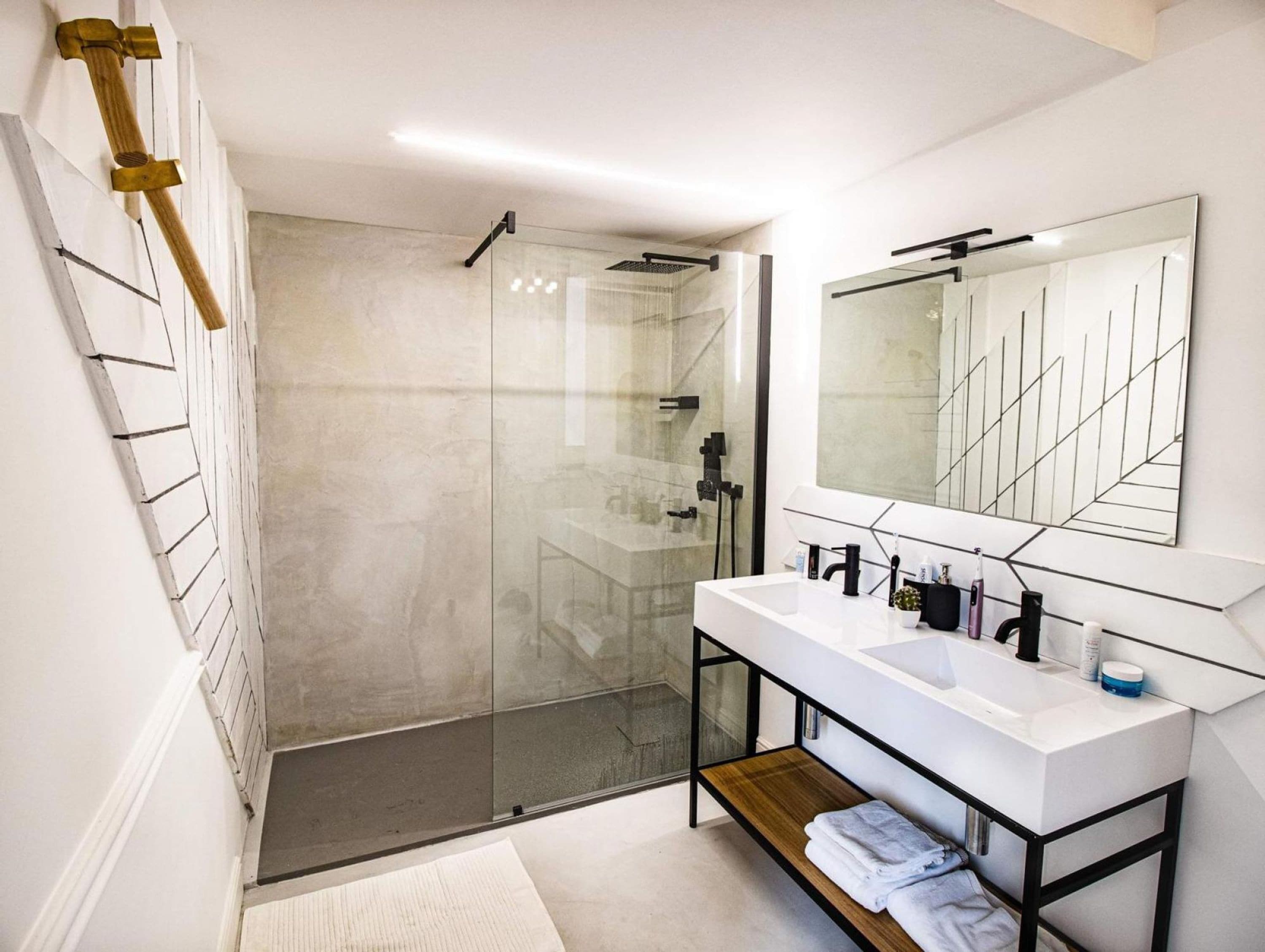 A modern bathroom with a glass-enclosed shower, a white vanity with a large mirror, and a wooden shelf with towels.