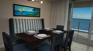 A dining area with a table set for four, a bench with a checkered pattern, and a painting of a tropical scene. - Marriott's Crystal Shores...The Perfect Getaway in this Luxurious 2 Bedroom (Marco Island)
