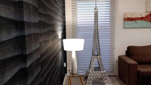 A modern living room with a patterned wall, a floor lamp, a decorative Eiffel Tower, and a brown sofa. - Be Haus Temporary Apartments (San Luis)