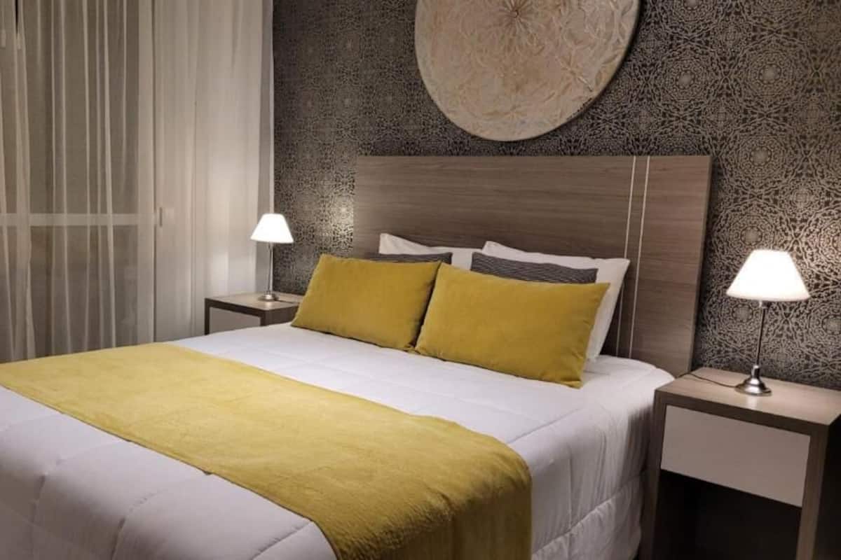 A neatly made bed with a yellow throw blanket, two bedside lamps, and a textured wall with a circular design above the bed.
